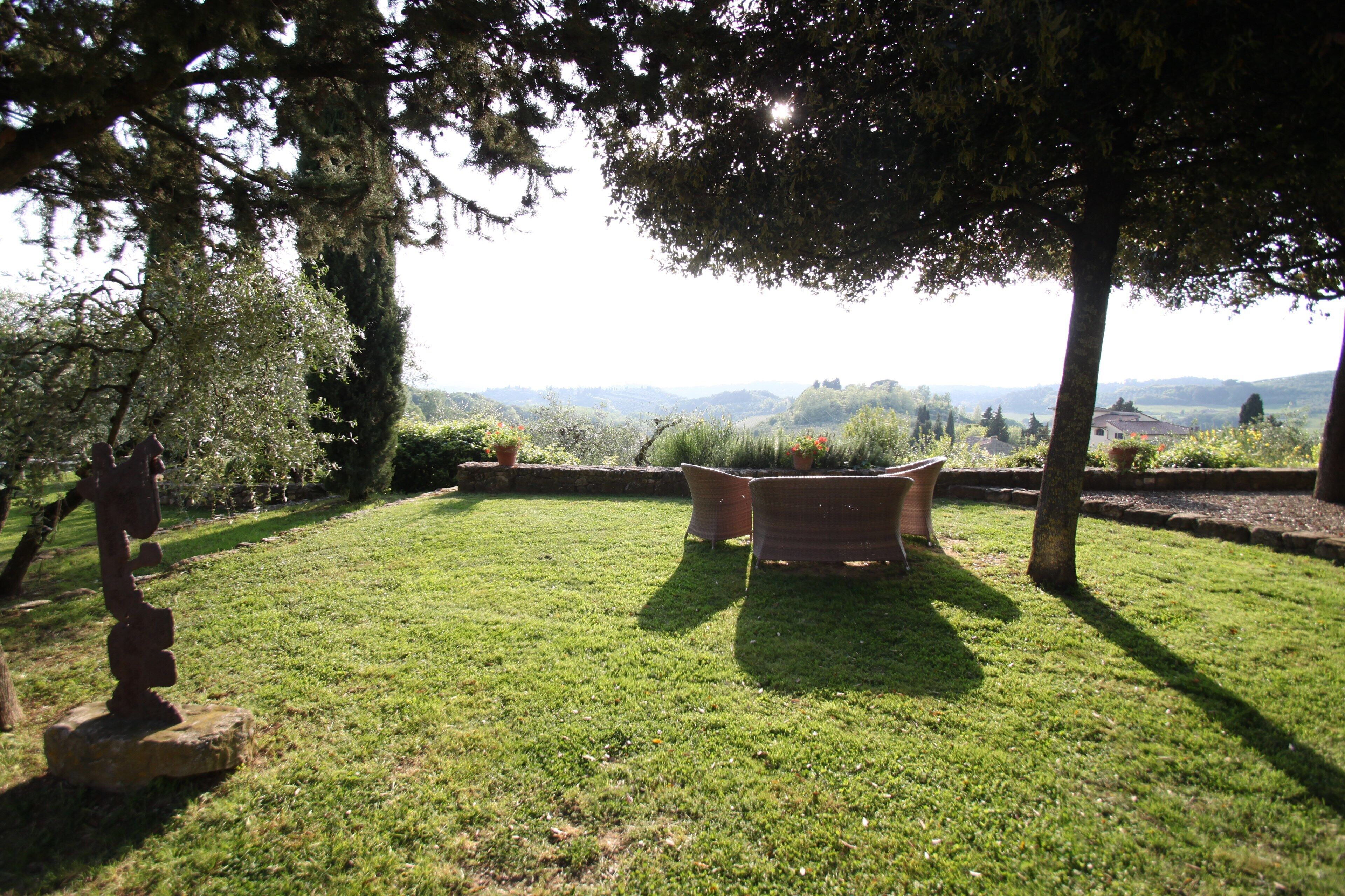 Un espace extérieur verdoyant, avec vue sur des collines lointaines, une sculpture en pierre et un banc en bois.