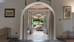 An arched doorway leading to an outdoor patio with a table and chairs, framed by a rustic wooden ceiling and a stone wall.
