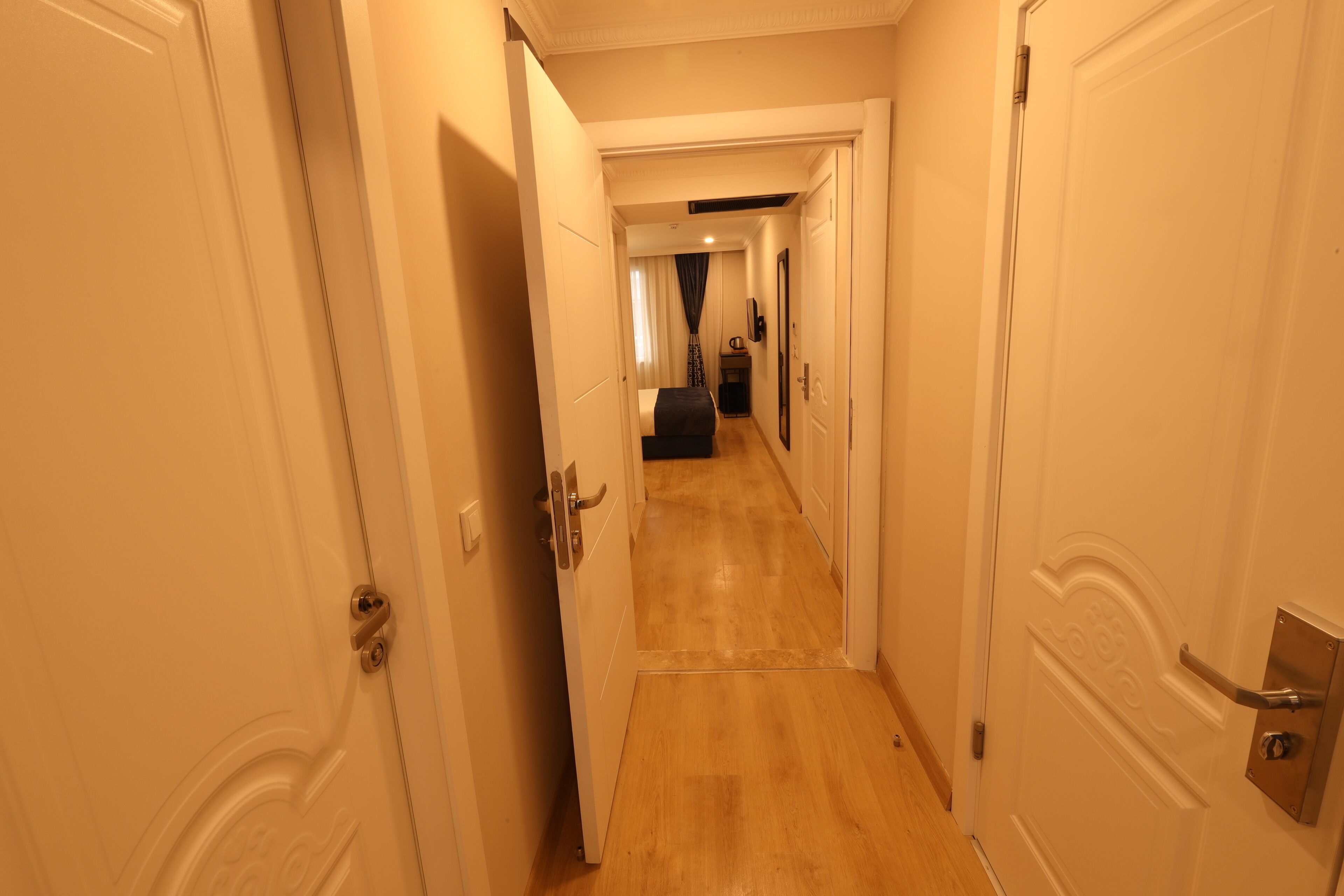 A narrow hallway with white doors and a wooden floor.