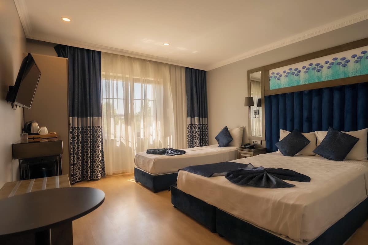 A hotel room with two beds, a desk, a TV, and a painting above the bed.