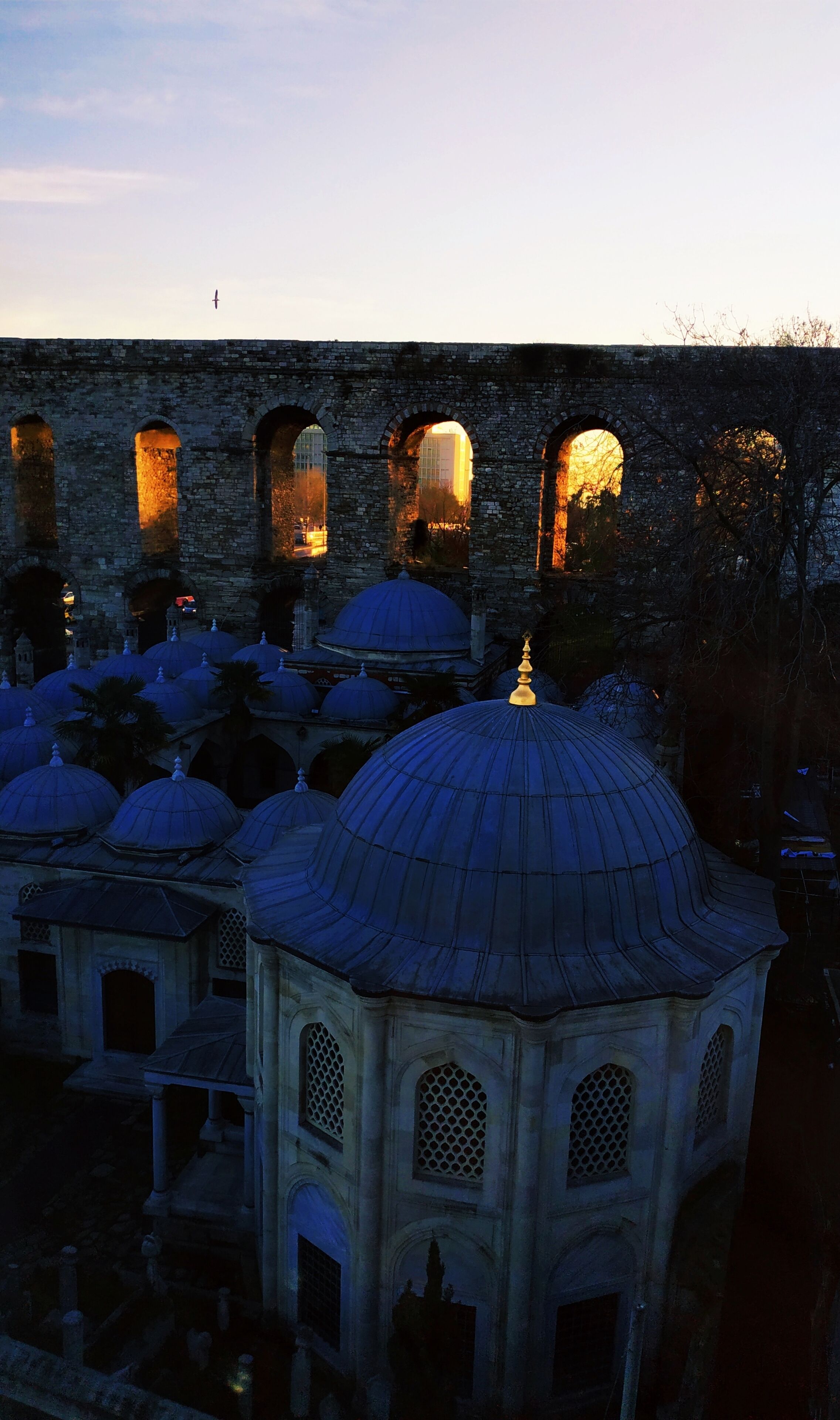 A historical building with multiple domes and arched windows, featuring stone walls and a prominent dome in the foreground.