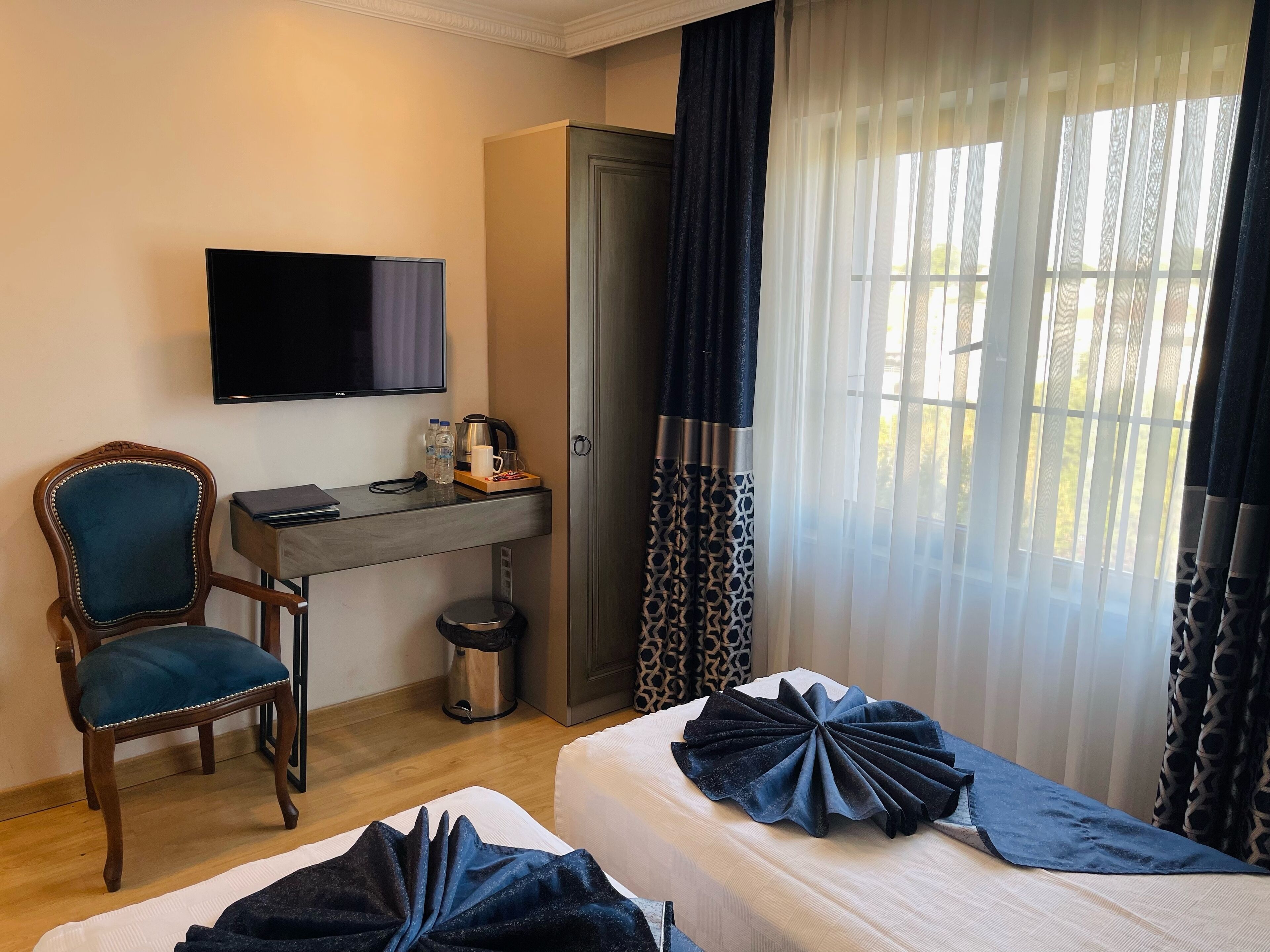 Una habitación de hotel con cama, escritorio con computadora, silla, televisor y cafetera.