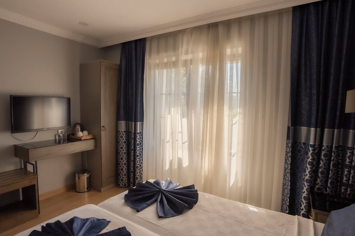 A hotel room with a bed, a TV, a bedside table with a lamp, and a wardrobe.
