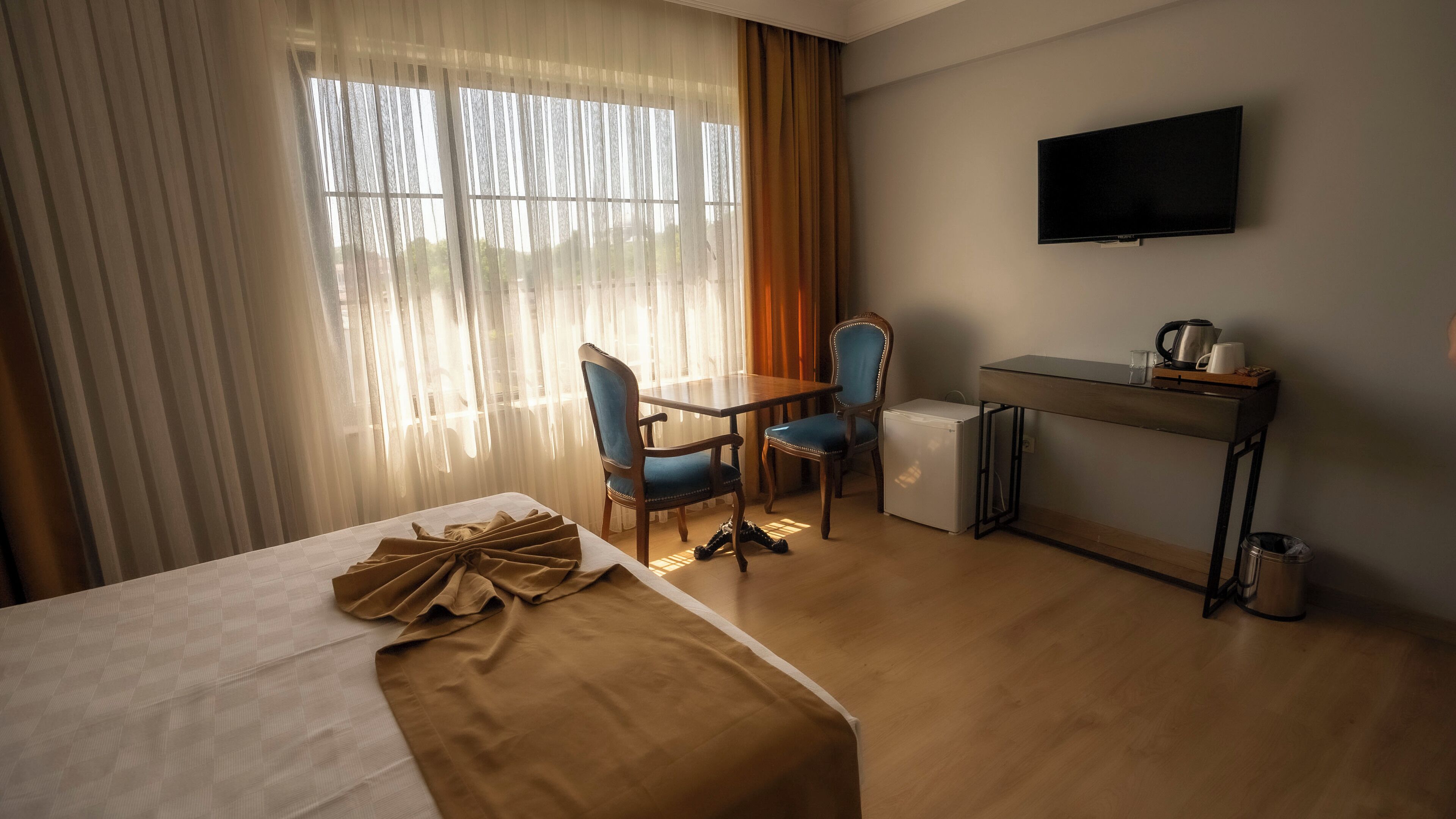 Une chambre d’hôtel équipée d’un lit, d’un bureau, de deux chaises, d’une télévision et d’un petit réfrigérateur.