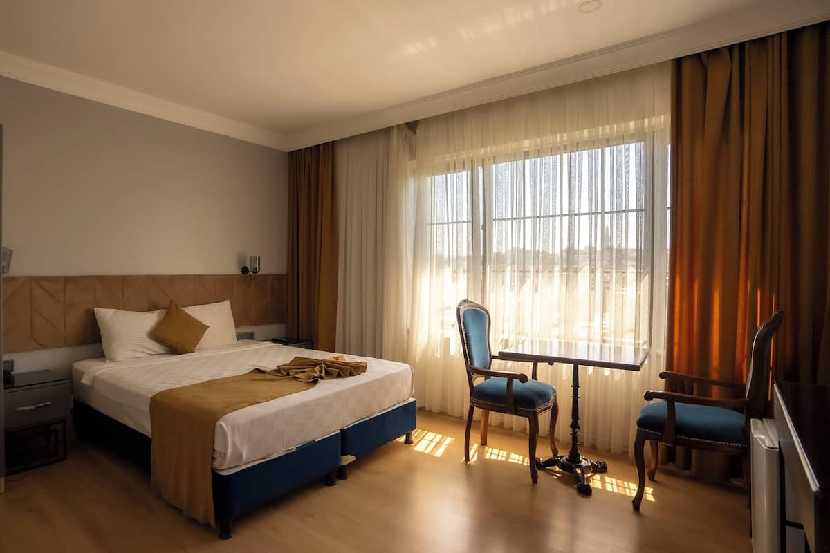 A hotel room with a bed, a desk, a chair, and a window with curtains.