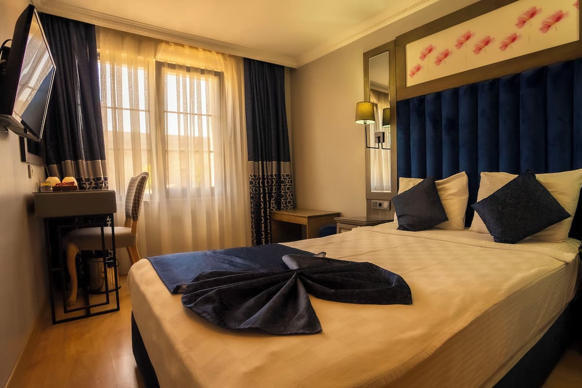 A hotel room with a bed, a desk, a chair, a lamp, and a mirror.