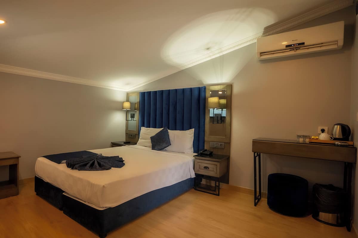 A hotel room with a bed, bedside tables, a mirror, a desk, and a trash bin.