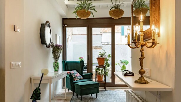 Uma sala de estar aconchegante com uma poltrona verde, uma mesinha de apoio branca e um vaso com planta.
