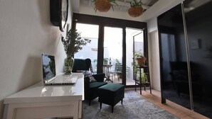Um espaço de escritório moderno com um laptop na mesa, uma cadeira verde, uma janela grande com vista e plantas penduradas.