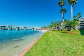 Hotel frente a la playa con vista despejada al océano, un puente y palmeras.