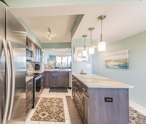 A modern kitchen with stainless steel appliances, a marble countertop island, and pendant lighting.
