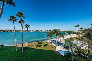 A resort with a pool, palm trees, a beach, and a bridge over water.