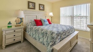 A bedroom with a bed, nightstands, a window with blinds, and a view of the outside.