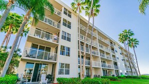 A multi-story hotel with balconies, a well-maintained lawn, and palm trees.