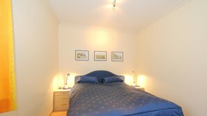 A bedroom with a bed, two bedside tables, and three framed pictures on the wall. - Becker House Alice 36 (Sylt)