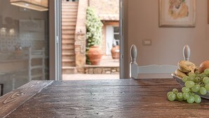 Ein Holztisch mit einer Schüssel grüner Trauben und Bananen, ein weißer Stuhl und ein Blick auf eine steinerne Treppe, die zu einem Außenbereich mit Blumentöpfen führt.