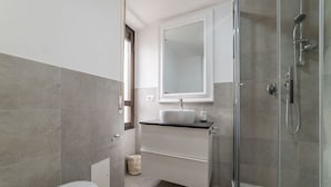 A bathroom with a toilet, a sink with a mirror, a shower, and a trash bin. - GuestHost - This comfortable 60 m2 apartment is located on the seventh and top floor (with a lift, which however is not suitable for the disabled) of a period building.The house is perfect for 4 peopleIt is located a few steps from Castel Sant'Angelo, cr (Roma)
