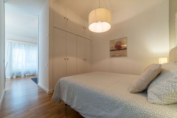 Un dormitorio con cama, armario, lámpara colgante y un cuadro en la pared.