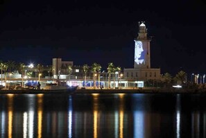 Een hotel aan het water met een opvallende toren, palmbomen en een kalm waterlichaam dat de lichten weerspiegelt.