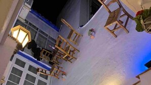 A room with a white exterior, a brick wall, and a window with a blue frame. There are wooden chairs and a table, and a lantern is visible. - Charming apartment in the center of Malaga (Málaga)