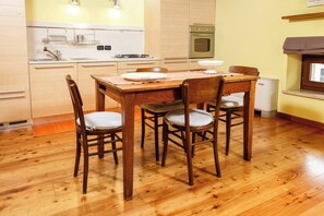 A kitchen with wooden flooring, a dining table with chairs, a stove, an oven, and a window with a curtain.