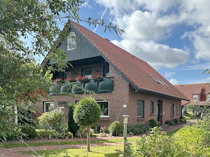 Een gebouw met twee verdiepingen, een schuin dak, bakstenen muren en een tuin ervoor.