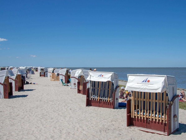 Beach huts with white canopies and wooden railings, lined up along a sandy beach.