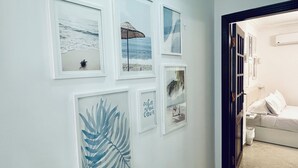 Een gang met ingelijste kunstwerken aan de muur, een bed met witte beddengoed en een betegelde vloer.