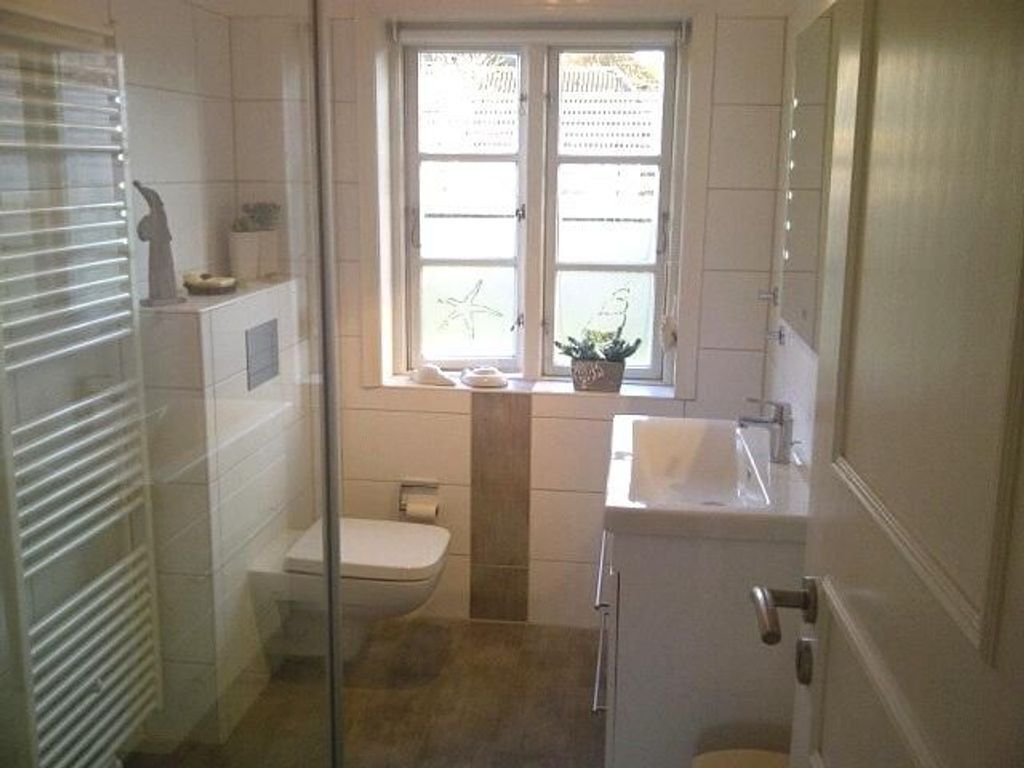 A bathroom with a toilet, a sink, and a window with a plant.