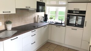 A modern kitchen with white cabinets, a black countertop, a built-in microwave, and a window with a view of greenery.