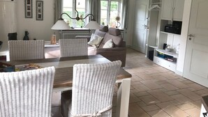 A spacious living area with a sofa, dining table, and chairs. There is a kitchen area with cabinets and a radiator.