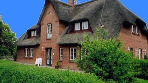 A traditional brick house with a thatched roof and multiple windows.