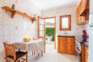 Una cocina con armarios de madera, una mesa de comedor con sillas y un ventanal con vistas a un jardín.