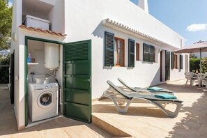 A compact, white building with a laundry area, a small outdoor seating area with lounge chairs, and a tiled patio.