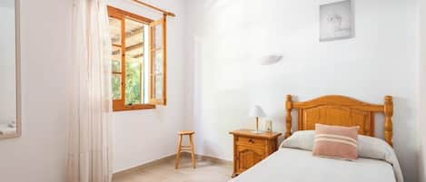 Ein Schlafzimmer mit einem hölzernen Bett, einem Nachttisch, einem kleinen Hocker und einem Fenster mit Vorhängen.