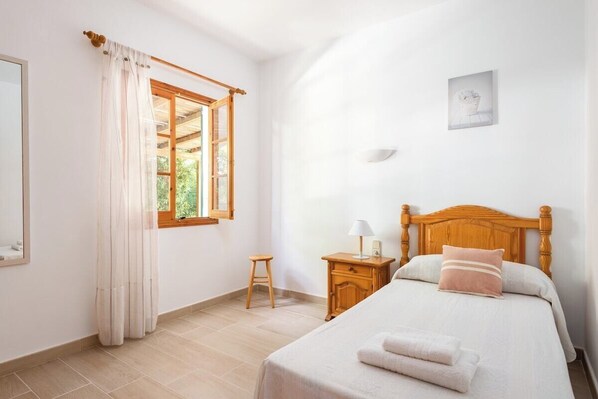 Une chambre à coucher avec un lit en bois, une table de chevet, un petit tabouret et une fenêtre avec des rideaux.