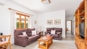 Ein geräumiges Wohnzimmer mit zwei Sofas, einem Holztisch, einem TV-Schrank und einem Essbereich mit Tisch und Stühlen.