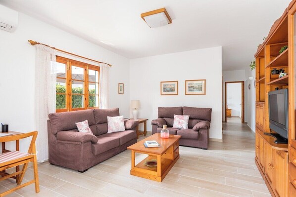 A spacious living room with two sofas, a wooden coffee table, a TV cabinet, and a dining area with a table and chairs.