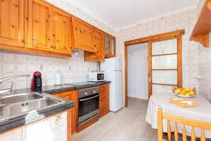 Een keuken met houten kastjes, een roestvrijstalen spoelbak, een magnetron en een koelkast.