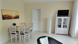 A living room with a dining area, a black leather chair, a TV on a cabinet, and a painting on the wall. - Große Str. 2 Möwe, apt. 29 (Wyk auf Föhr)