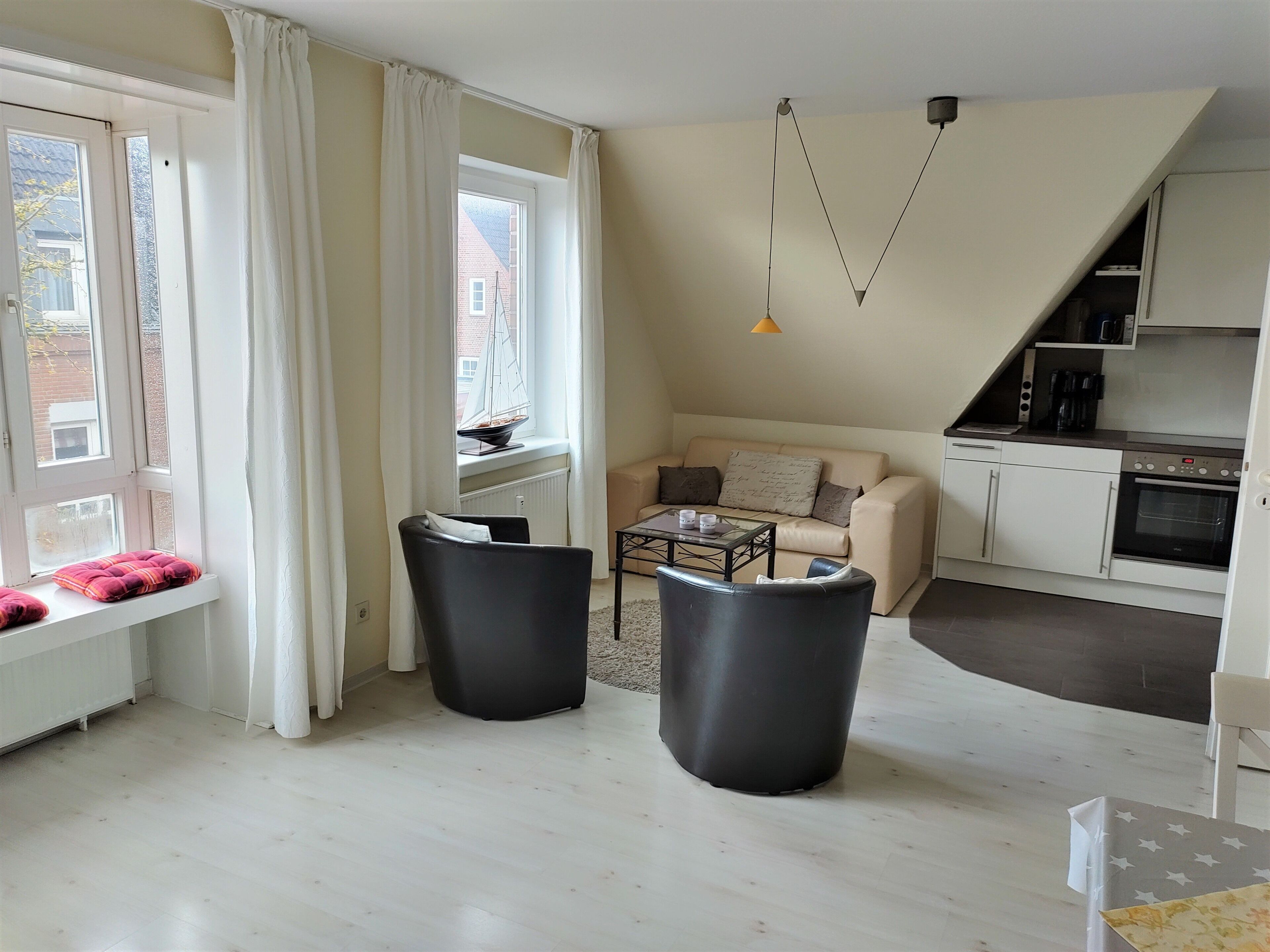 A modern living room with a sofa, two black chairs, a coffee table, and a view of the city through large windows.