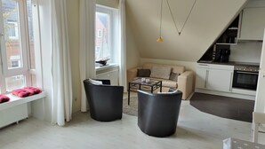 A modern living room with a sofa, two black chairs, a coffee table, and a view of the city through large windows. - Große Str. 2 Möwe, apt. 29 (Wyk auf Föhr)