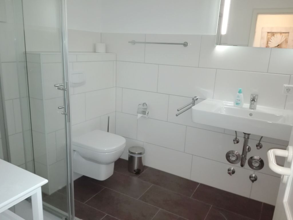 Un baño moderno con cabina de ducha de vidrio, inodoro blanco, lavabo con espejo y un cubo de basura.