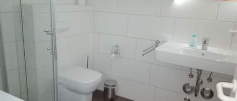 Un baño moderno con cabina de ducha de vidrio, inodoro blanco, lavabo con espejo y un cubo de basura.