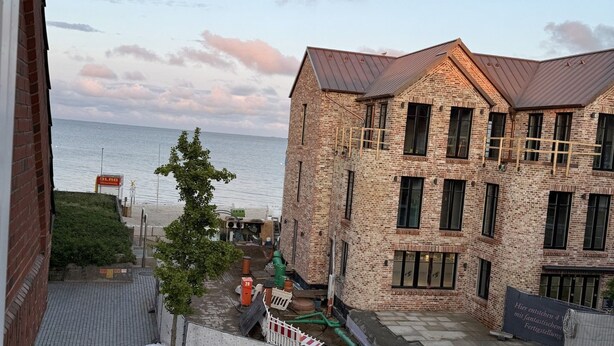 A view of a building with a brick facade and a metal roof, situated next to a body of water. - Große Str. 2 Möwe, apt. 29 (Wyk auf Föhr)