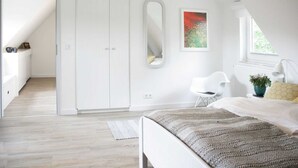 Ein Schlafzimmer mit einem Bett, einem Kleiderschrank, einem Spiegel, einem Sessel und einem Fenster.