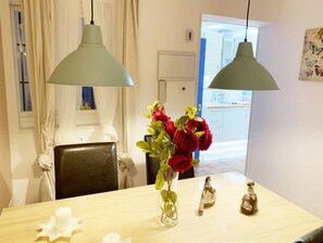 A dining area with a wooden table, two pendant lights, a vase with red roses, and a small decorative figure.