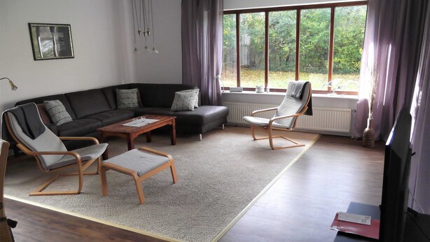 Una sala de estar moderna con un sofá seccional, dos sillones, una mesa de centro y un ventanal con cortinas.