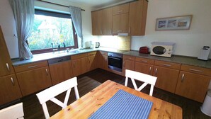 Una cocina funcional con muebles de madera, una mesa de madera y un ventanal con cortinas.