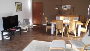 Una sala de estar con televisión, asientos, una mesa de comedor y piso de madera.